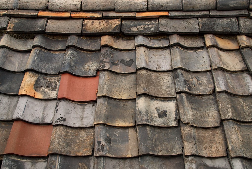 A single replacement tile among older weathered roof tiles